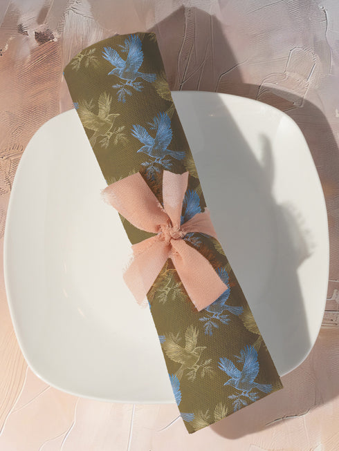 Set of four golden cloth napkins featuring alternating powder blue and metallic gold ravens in flight, sized 18x18 inches.